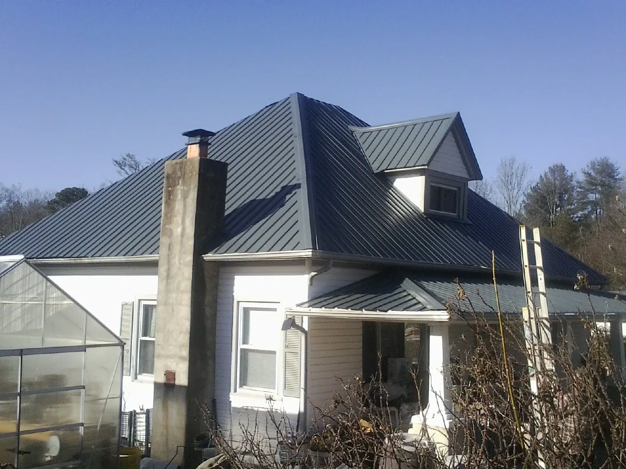 Dark blue standing seam metal roof on a white farmhouse with dormer — Slate & Tile Roof Repair by Roofing Brothers in Germantown
