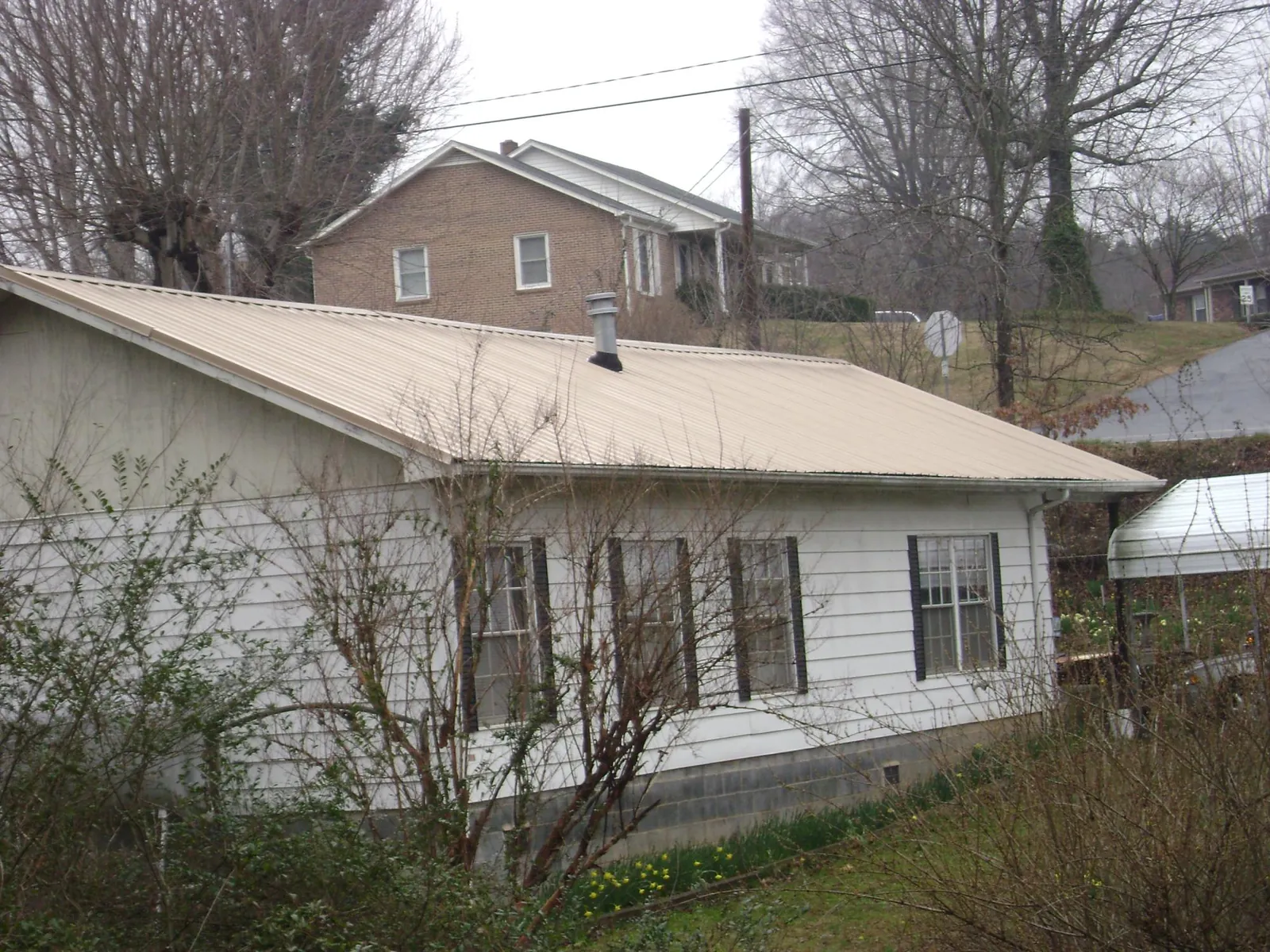 Tan metal roof on a white sided house set into a hillside — Commercial Roofing by Roofing Brothers in Germantown